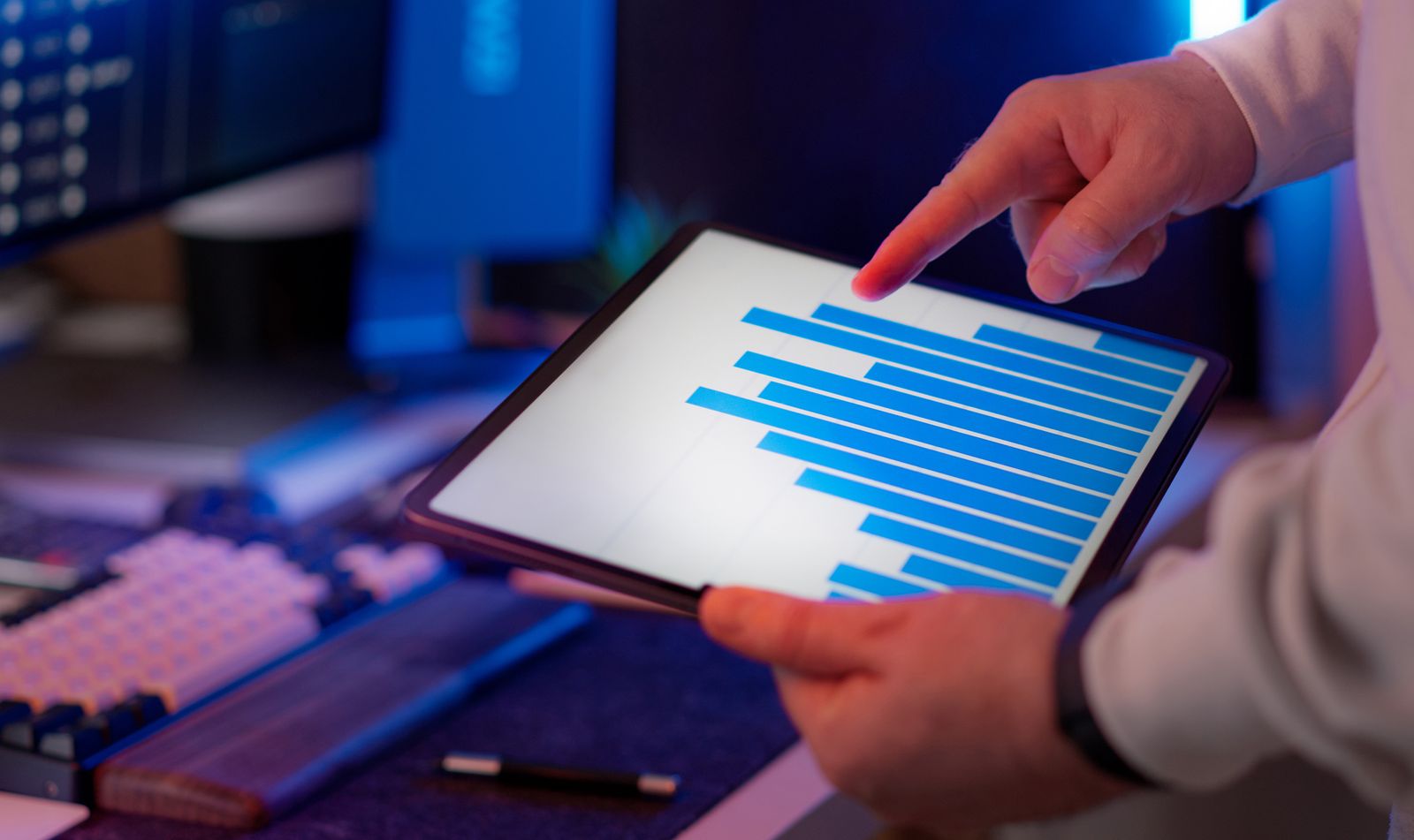 Close-up of a hand pointing at a bar chart analytics dashboard on a tablet