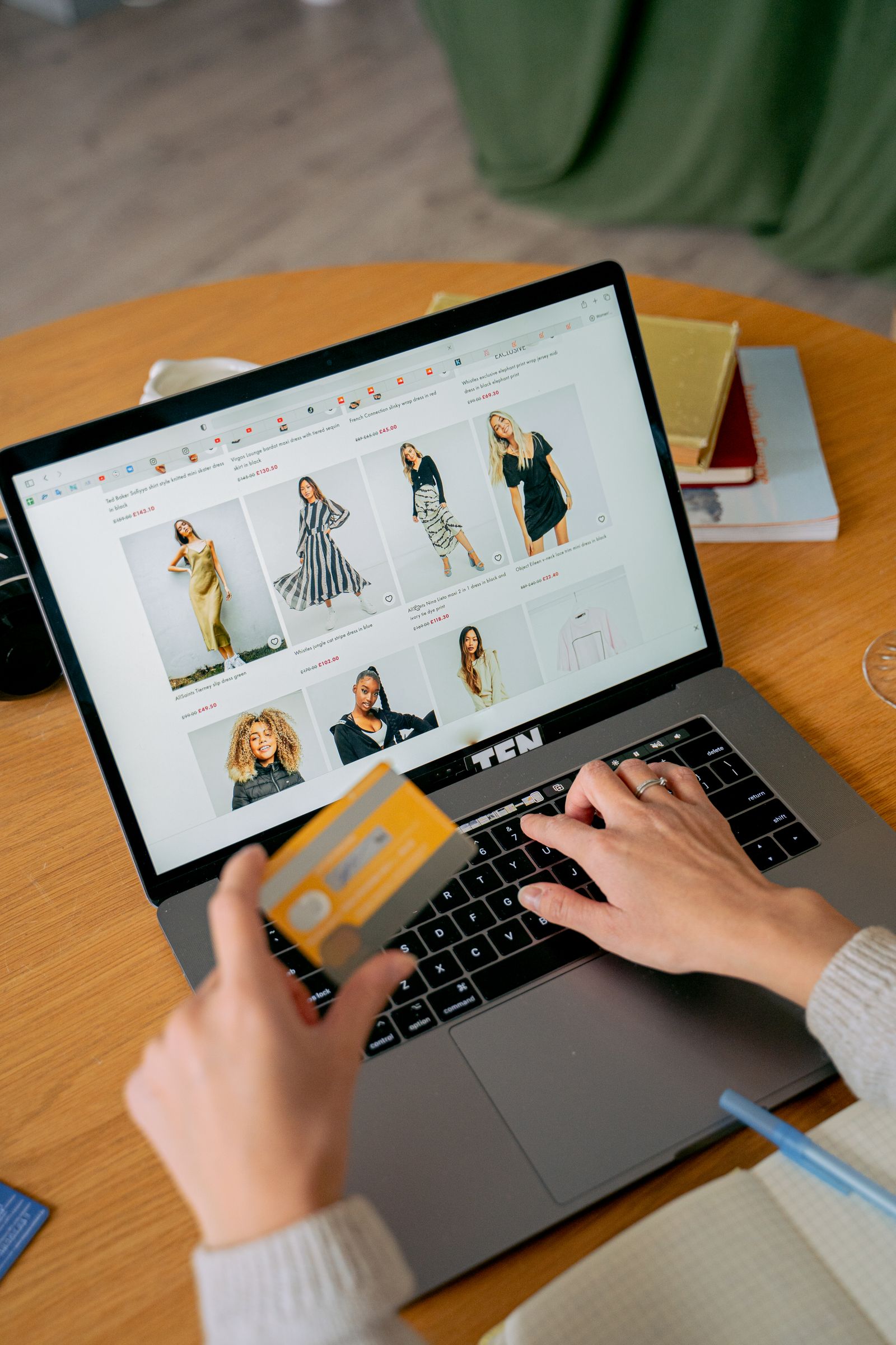 A customer browsing an online clothing store and holding a payment card on a laptop