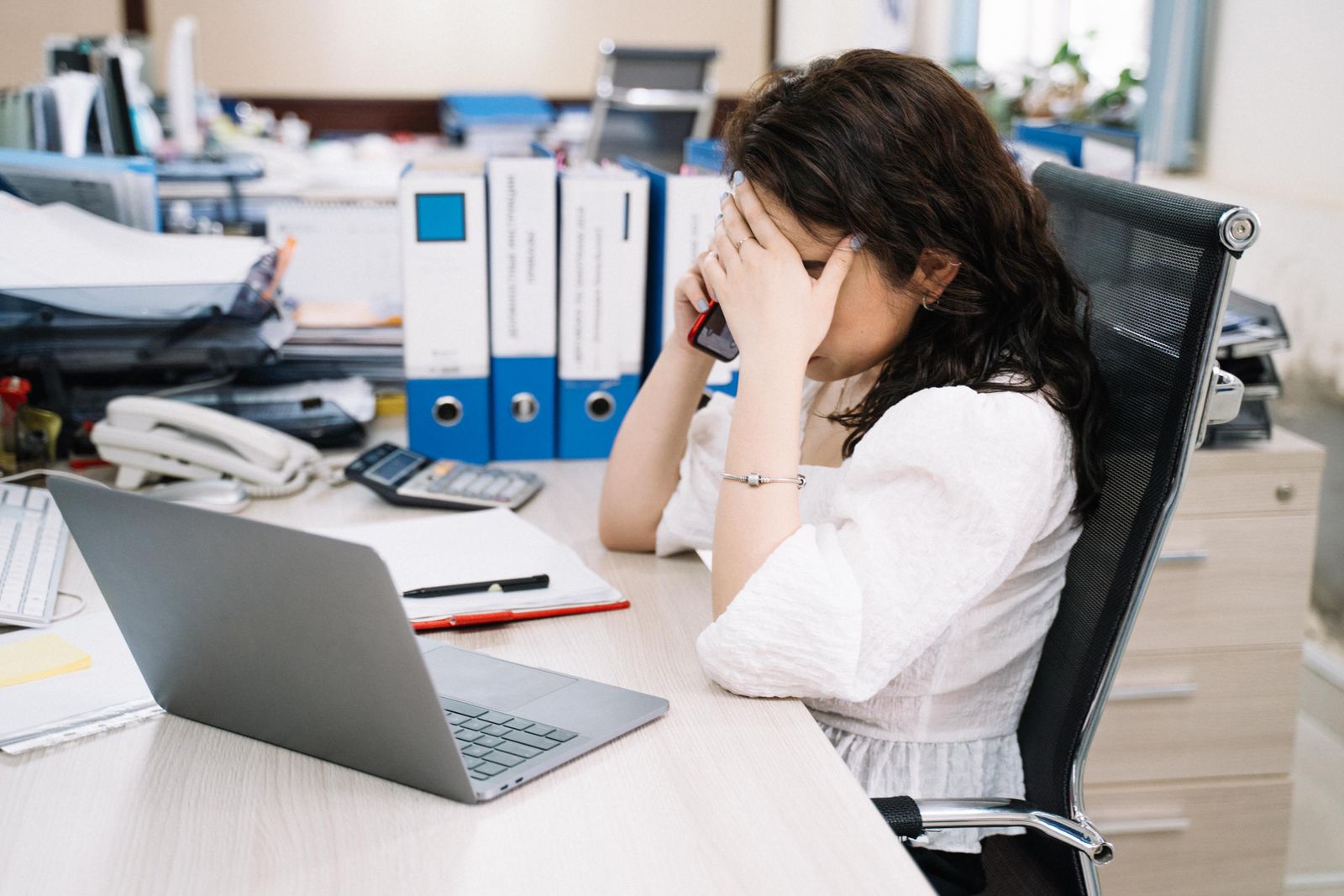 A stressed business owner on the phone at her desk trying to resolve an issue
