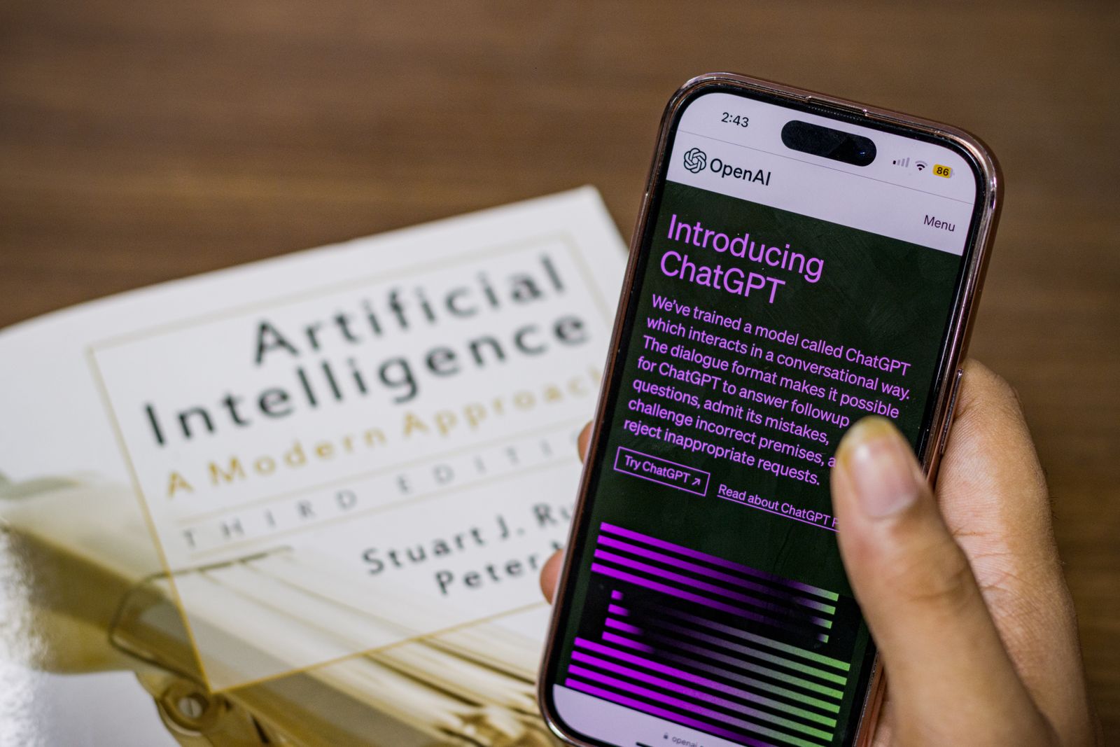 Phone screen showing OpenAI's Introducing ChatGPT announcement page next to an AI textbook